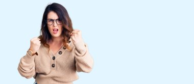 Güzel, genç, esmer bir kadın, günlük kıyafetler ve gözlükler takıyor kızgın ve kızgın yumruklar sallıyor öfkeyle bağırırken sinirli ve öfkeli. öfke ve agresif konsept. 