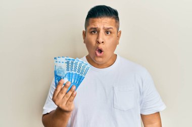 On bin Şili pezosu elinde tutan genç Latin adam şaşkınlık ve şaşkınlık içinde ağzı açık kaldı. 