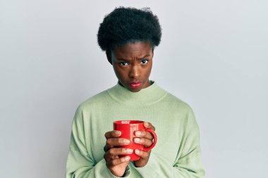 Afro-Amerikalı genç bir kız bir fincan kahve içiyor şüpheci ve gergin, sorun yüzünden surat asıyor. negatif kişi. 