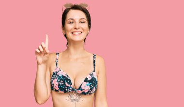 Kısa saçlı, bikini giyen esmer bir kadın başarılı bir fikirle işaret ediyor. Heyecanlı ve mutlu. Bir numara.. 