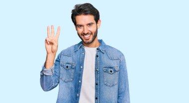 Gündelik kıyafetler giyen genç İspanyol adam üç numarayı gösterip işaret ederken kendinden emin ve mutlu gülümsüyor.. 