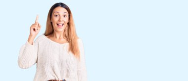 Gündelik giysiler giymiş güzel genç bir kadın başarılı bir fikirle işaret ediyor. Heyecanlı ve mutlu. Bir numara.. 