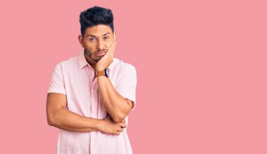 Yakışıklı Latin Amerikalı genç adam rahat bir yaz gömleği giyiyor. Kollarını kavuşturup depresyondan sıkılmış ve yorgun görünüyor.. 