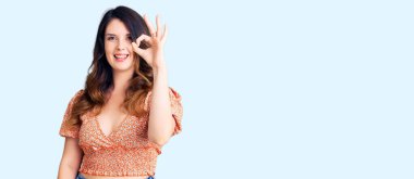 Güzel, genç, esmer, günlük kıyafetler giyen, gülümseyen, el ve parmaklarıyla 