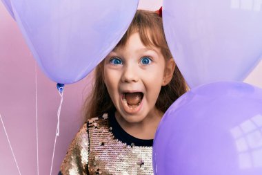 Küçük beyaz kız elinde balonlarla çılgınlığı kutluyor ve başarıya hayret ediyor gözleri açık heyecanla haykırıyor. 