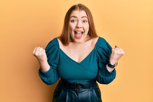 Young beautiful redhead woman wearing elegant and sexy look celebrating surprised and amazed for success with arms raised and open eyes. winner concept. 