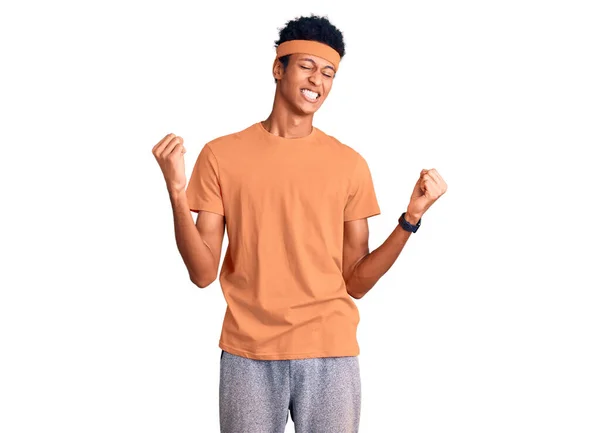 スポーツウェアを身に着けている若いアフリカ系アメリカ人の男性は非常に満足し 腕を上げて勝者のジェスチャーを行う興奮し 笑顔と成功のために叫んでいる お祝いのコンセプト — ストック写真