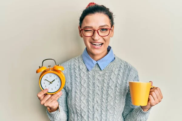 Young Caucasian Woman Holding Alarm Clock Drinking Coffee Winking Looking — 图库照片