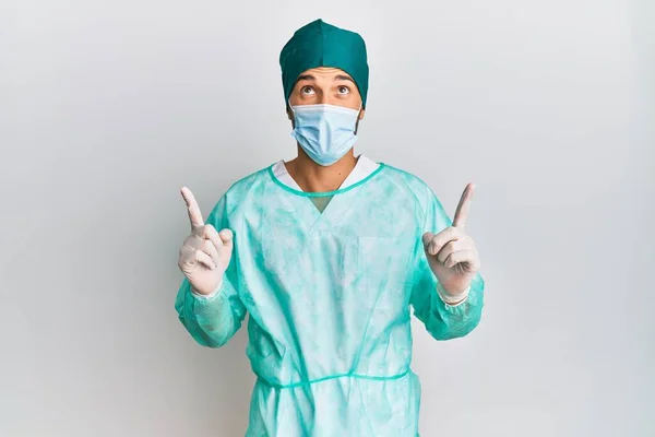 Fiatal Jóképű Férfi Sebész Egyenruhában Orvosi Maszkban Csodálkozva Meglepve Nézett — Stock Fotó