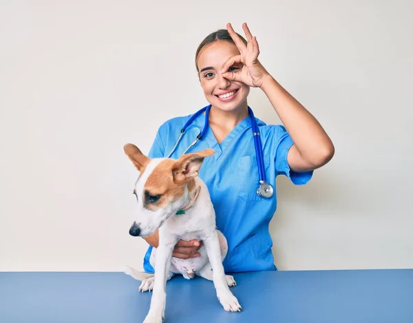 若いです美しいですブロンド獣医師の女性チェック犬の健康笑顔幸せな行いますOk Signとともに手で目を通して指 — ストック写真