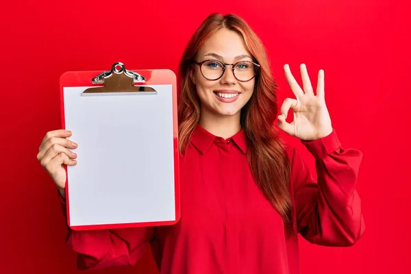 Joven Pelirroja Sosteniendo Portapapeles Con Espacio Blanco Haciendo Signo Con — Foto de Stock