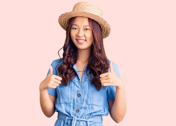 年轻美丽的中国姑娘戴着夏帽 成功地做了一个积极的手势 微笑着竖起大拇指 快乐地微笑着 快乐的表达和胜利的姿态 — 图库照片