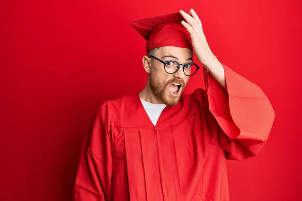 Young Redhead Man Wearing Red Graduation Cap Ceremony Robe Surprised — Stock Photo, Image