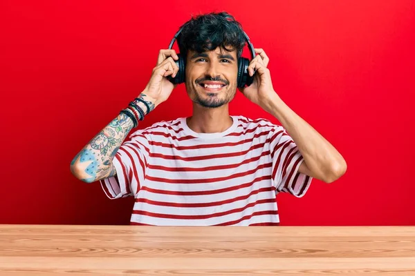 Junger Hispanischer Mann Mit Kopfhörern Der Auf Dem Tisch Sitzt — Stockfoto