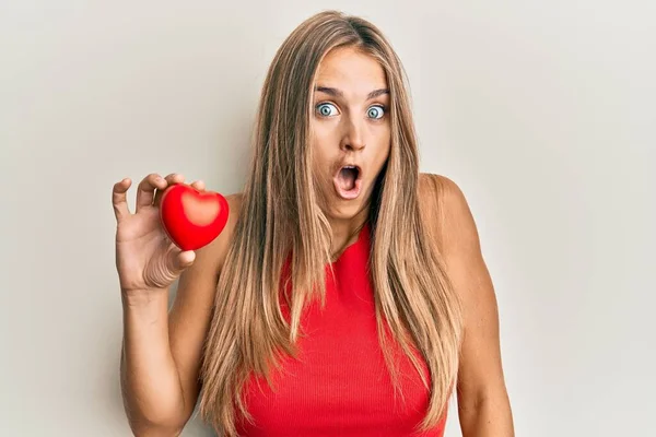 Young Blonde Woman Holding Heart Scared Amazed Open Mouth Surprise — 图库照片