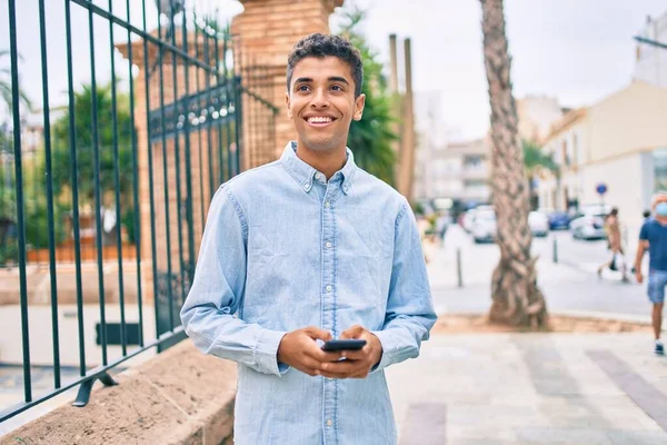 Νεαρός Λατίνος Άνθρωπος Χαμογελώντας Χαρούμενος Χρησιμοποιώντας Smartphone Περπάτημα Στην Πόλη — Φωτογραφία Αρχείου
