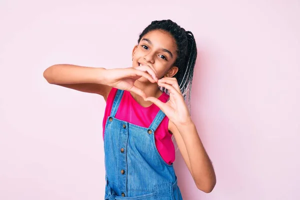 手でハートのシンボルの形をする愛に笑顔ピンクの背景の上にカジュアルな服を身に着けているブライドを持つ若いアフリカ系アメリカ人の女の子の子供 ロマンチックなコンセプト — ストック写真