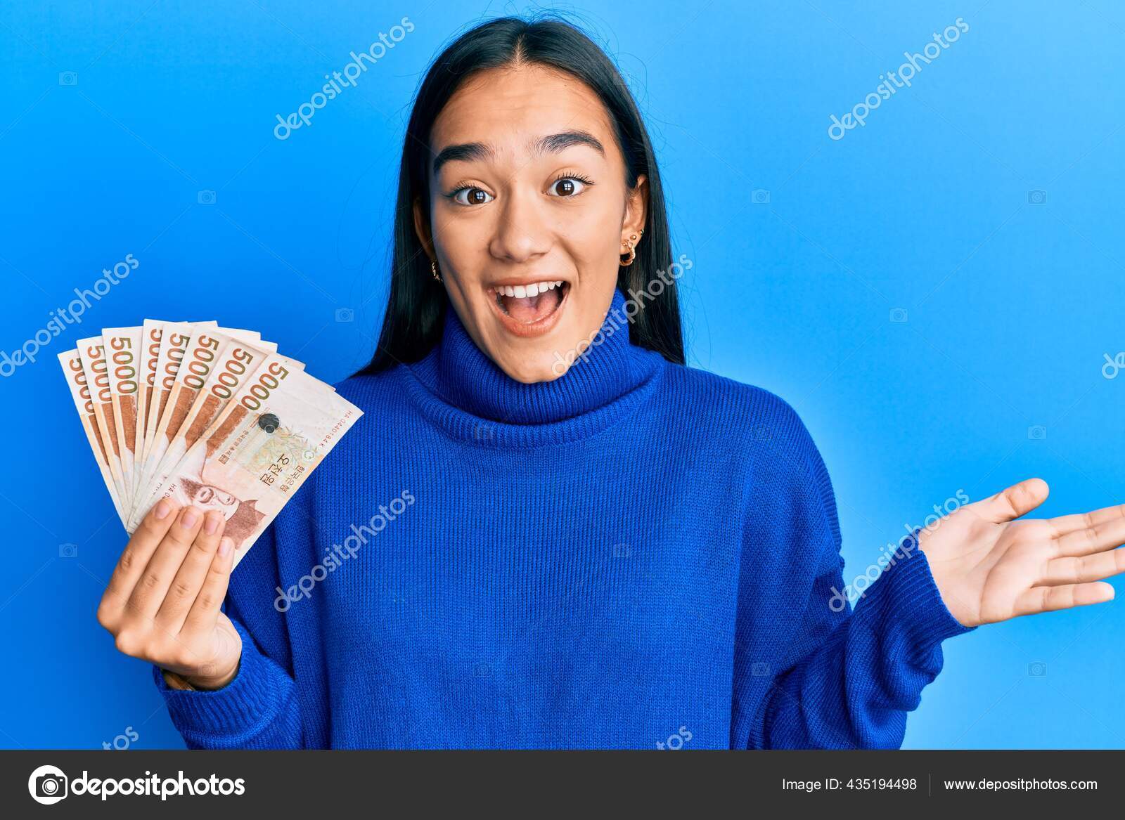 年轻的亚洲女人手持5000韩元的韩元钞票笑容满面高举双手庆祝胜利——图库图片© Krakenimages.com #435194498