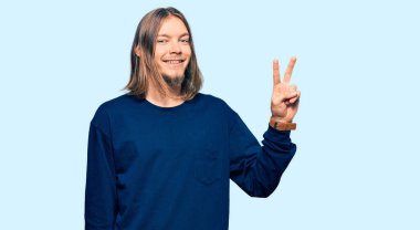 Uzun saçlı, sıradan bir kazak giyen yakışıklı beyaz adam kameraya bakıp zafer işareti yaparken gülümsüyor. İki numara.. 