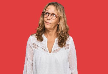 Orta yaşlı, beyaz gömlek ve gözlük takan sarışın bir kadın gülümsüyor.. 