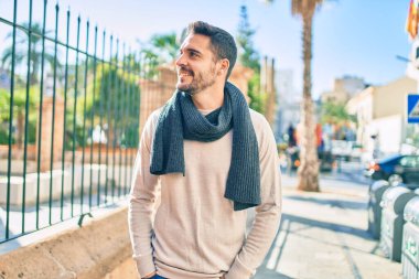 Şehre yürürken atkı takan, mutlu gülümseyen genç İspanyol adam..