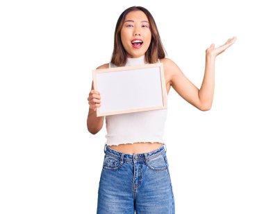 Genç, güzel Çinli kız elinde boş beyaz karatahta ile zaferi kutluyor mutlu bir gülümseme ve ellerini kaldırarak kazanan bir ifadeyle. 