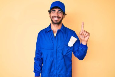 Kıvırcık saçlı ve ayı gibi giyinmiş yakışıklı genç adam bir numarayı gösterip gösterirken kendinden emin ve mutlu bir şekilde gülümsüyor.. 