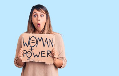 Genç, güzel bir kadın elinde güç pankartı tutuyor. Korkmuş ve hayrete düşmüş bir şekilde ağzı açık, şaşırmış bir halde. 