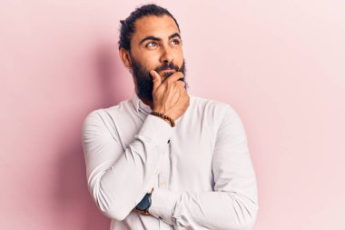 Elleri çenesinde gündelik giysiler giyen genç bir Arap sorgulamayı, düşünceli bir ifadeyi düşünüyor. Düşünceli bir yüzle gülümsüyor. şüphe kavramı. 