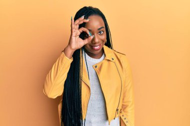 Genç Afro-Amerikalı kadın günlük ceket giyiyor. El hareketleriyle gülümsüyor, gözleriyle mutlu yüzüyle parmaklarının arasından bakıyor.. 