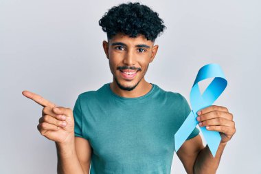 Genç Arap yakışıklı adam mavi kurdele tutuyor gülümsüyor mutlu eli ve parmağı yana bakıyor 