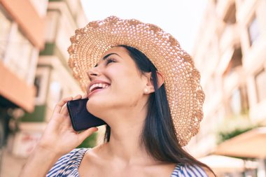 Tatildeki genç Latin turist kız gülümseyerek şehirde akıllı telefondan konuşuyor..