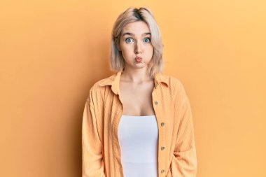 Sıradan kıyafetler giyen genç sarışın kız komik yüzlü yanakları şişiriyor. Havayla şişmiş ağız, çılgın bir ifade.. 