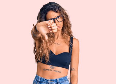 Dövmeli, sıradan kıyafetler giyen, gözlüklü, mutsuz görünen, reddedilmiş, olumsuz jestli genç İspanyol bir kadın. kötü ifade. 