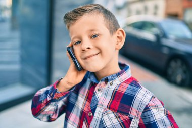 Sevimli beyaz çocuk gülümsüyor. Şehirdeki akıllı telefondan konuşuyor..