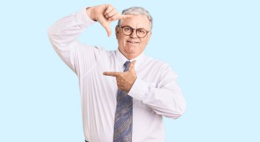 Kıdemli gri saçlı, iş kıyafetleri giyen, gülümseyen, elleri ve parmakları gülen yüzlü bir adam. yaratıcılık ve fotoğrafçılık kavramı. 