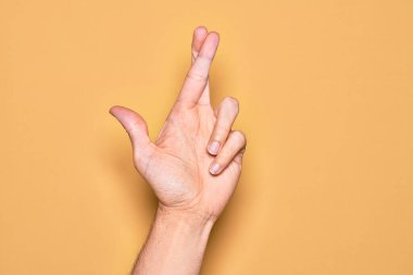 Kafkas genci parmaklarını izole edilmiş sarı arka plan üzerinde gösteriyor. Parmaklarını çapraz yapıyor, batıl inançlar ve şanslı bir jest, şanslı ve umut dolu bir ifade.