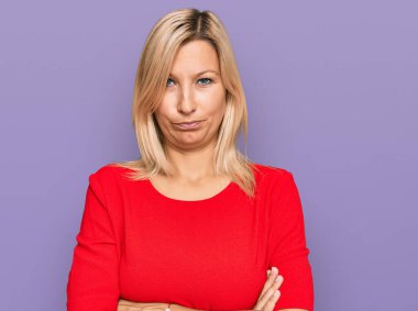 Orta yaşlı beyaz kadın, gündelik kıyafetler giyiyor şüpheci ve gergin, yüzünde çapraz kollu tasvip etmeyen bir ifade var. negatif kişi. 