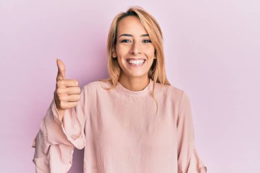 Kış süveteri giyen güzel sarışın kadın mutlu ve pozitif gülümsüyor, başparmağıyla mükemmel ve onay işareti yapıyor. 