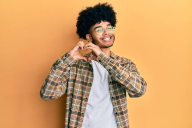 Afro saçlı, sıradan kıyafetler giyen, aşık bir şekilde gülümseyen, elleriyle kalp sembolü çizen genç Afro-Amerikan bir adam. romantik kavram. 