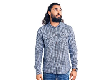 Gündelik kıyafetler giyen genç Arap adam gülümsüyor, yan tarafa bakıyor ve düşünüyor.. 