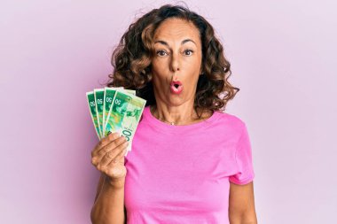 Orta yaşlı İspanyol kadın İsrail şekellerini tutuyor. Şaşırtmak için ağzı açık kalmış, korkmuş ve hayrete düşmüş. İnanmayan yüz. 