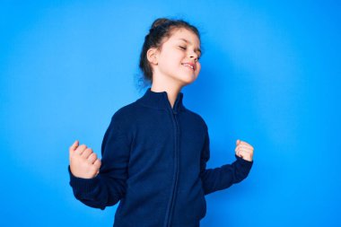 Sevimli İspanyol çocuk gündelik kıyafetler giyiyor. Çok mutlu ve heyecanlı. Kazanan jest yapıyor, kollarını kaldırıyor, gülümsüyor ve başarı için bağırıyor. kutlama konsepti. 