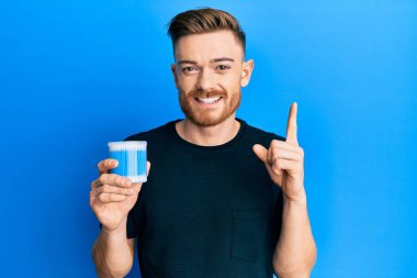 Kulak kiri temizleyici tutan genç kızıl saçlı adam bir fikir veya soruyla gülümsüyor ve mutlu bir yüzle işaret ediyor. 