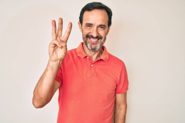 Orta yaşlı İspanyol bir adam gündelik giysiler giyip üç numarayı gösterip işaret ederken kendinden emin ve mutlu bir şekilde gülümsüyor.. 