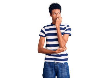 Gündelik kıyafetler giyen genç Afro-Amerikan bir adam gergin görünüyor ve elleri ağzında tırnak yiyor. anksiyete. 