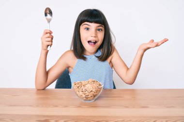 Bangır bangır küçük bir kız masada oturmuş mısır gevreği yiyor başarıyı mutlu bir gülümsemeyle kutluyor ve kazanan el kaldırarak ifade ediyor. 