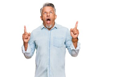 Orta yaşlı, gri saçlı, sıradan kıyafetler giyen, hayrete düşmüş, şaşırmış, parmaklarıyla işaret eden ve kollarını kaldıran bir adam.. 