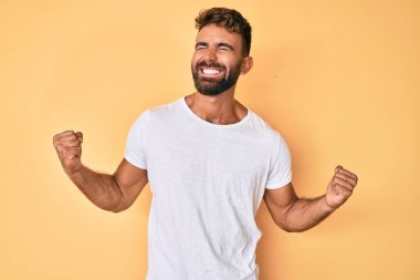 Gündelik kıyafetler giyen genç İspanyol adam çok mutlu ve heyecanlı. Kazanan jestler yapıyor. Kolları havada, gülümsüyor ve başarı için bağırıyor. kutlama konsepti. 