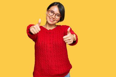 Kısa saçlı, günlük süveter giyen ve gözlük takan genç, güzel İspanyol bir kadın. Elleriyle olumlu bir jest yapıyor, gülümsüyor ve başarı için seviniyor. kazanan jest. 